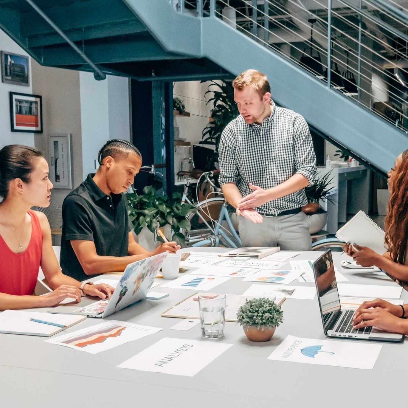 six people discussing at a table with laptops and papers